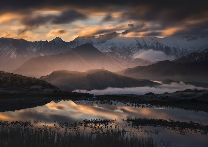 Mountain photographer captures colorful fall in the Alps with dramatic clouds and reflection in a calm lake at sunset.