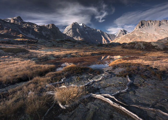 Alps mountain landscape in fall with colorful foliage, rocky terrain, and dramatic cloudy sky at sunset.