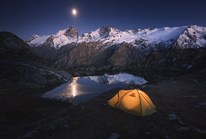 Yellow tent illuminated at night beside a lake reflecting snowy Alps mountains, showcasing colorful fall mountain photography.