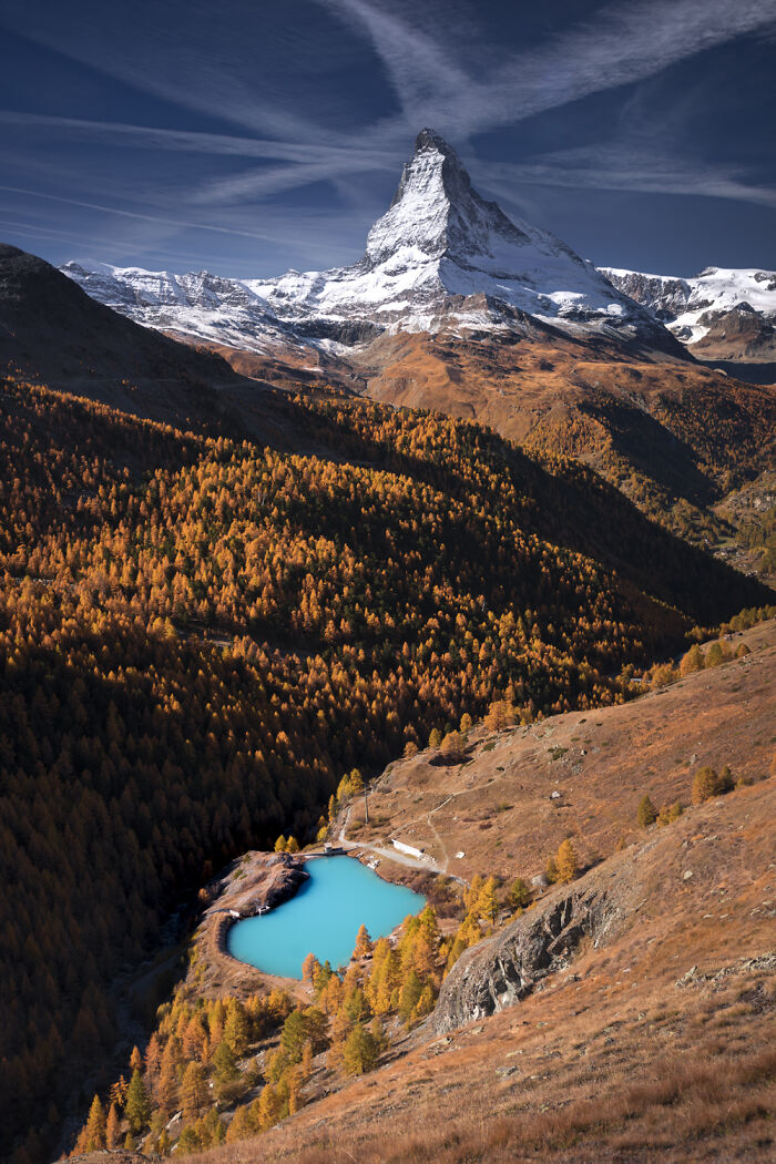 Snow-capped mountain peak and vibrant fall colors in the Alps with a bright blue alpine lake below.