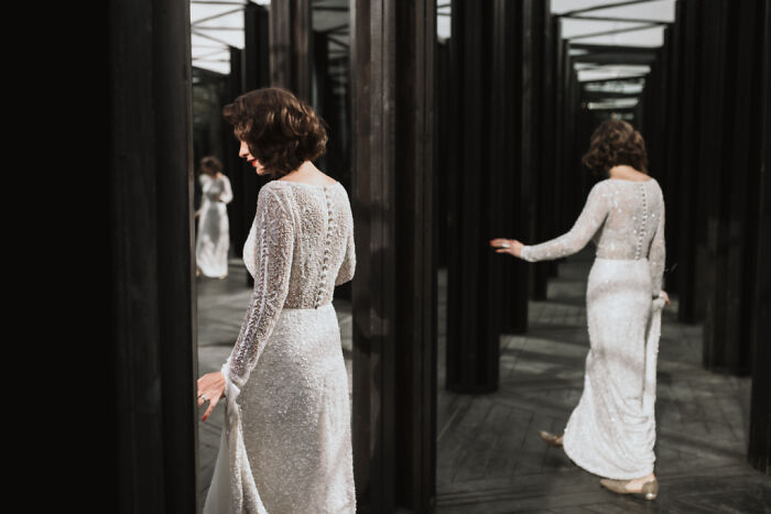 Bride in a lace wedding dress standing among mirrors, captured in a top submission to the 2021 wedding photographer competition.