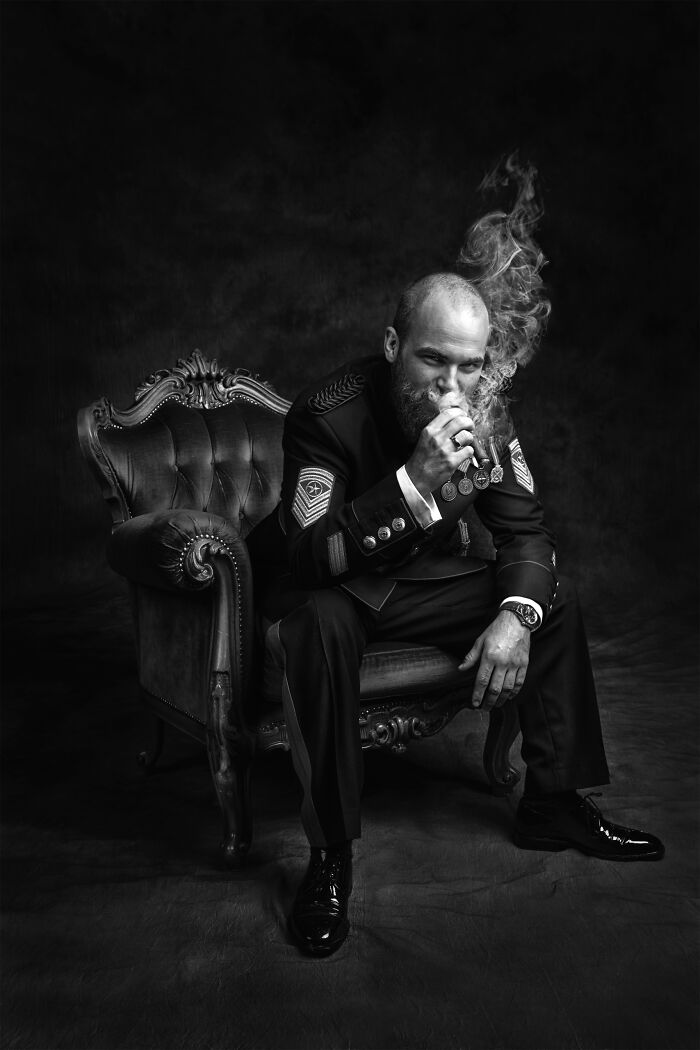 Black and white portrait of a bearded man in formal attire sitting on an antique chair, featured in wedding photographer contest.