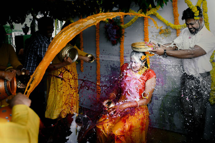 Bride joyfully showered with colorful powders and liquids during vibrant ceremony, captured in International Wedding Photographer of the Year submissions.