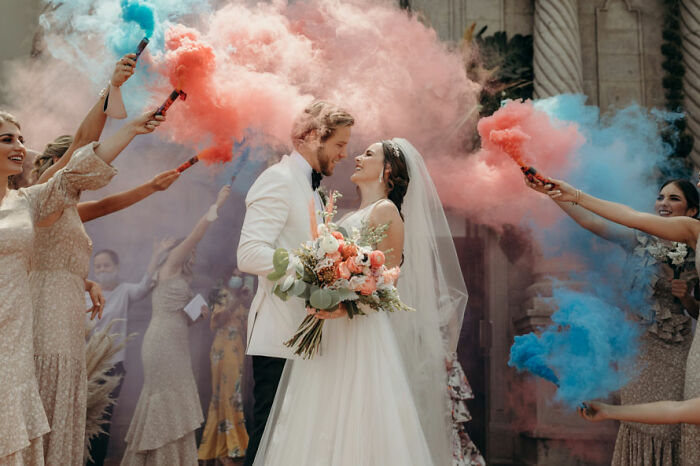 Bride and groom surrounded by bridesmaids holding colorful smoke bombs in a vibrant wedding photographer competition submission.