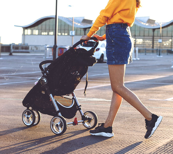 Person in denim skirt and sneakers pushing a stroller outdoors, reflecting Disney theme park employees' daily experiences.