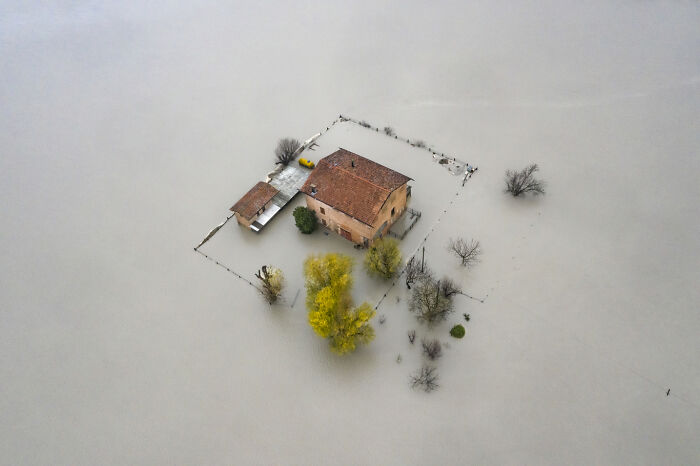 Aerial view of a flooded house surrounded by water and trees, showcasing impactful environmental photography.