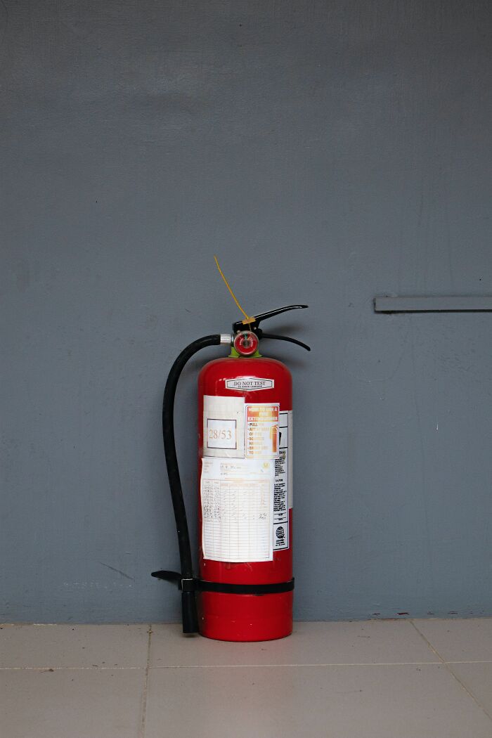 Red fire extinguisher against a gray wall, illustrating tips on where burglars say you should never hide your stuff.