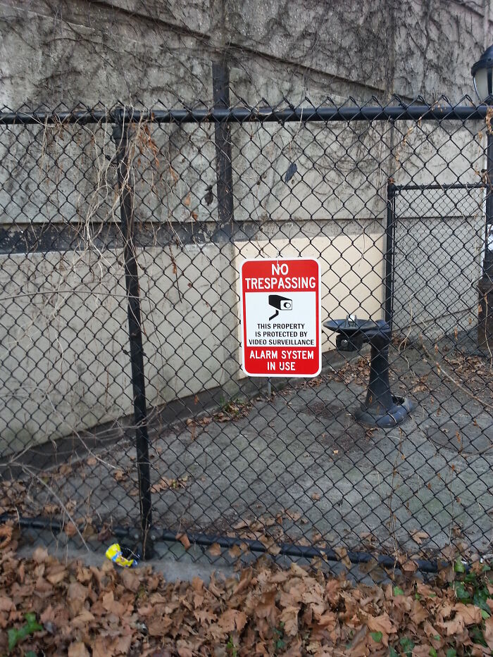 Chain-link fence with no trespassing sign warning about video surveillance and alarm system to prevent burglary.
