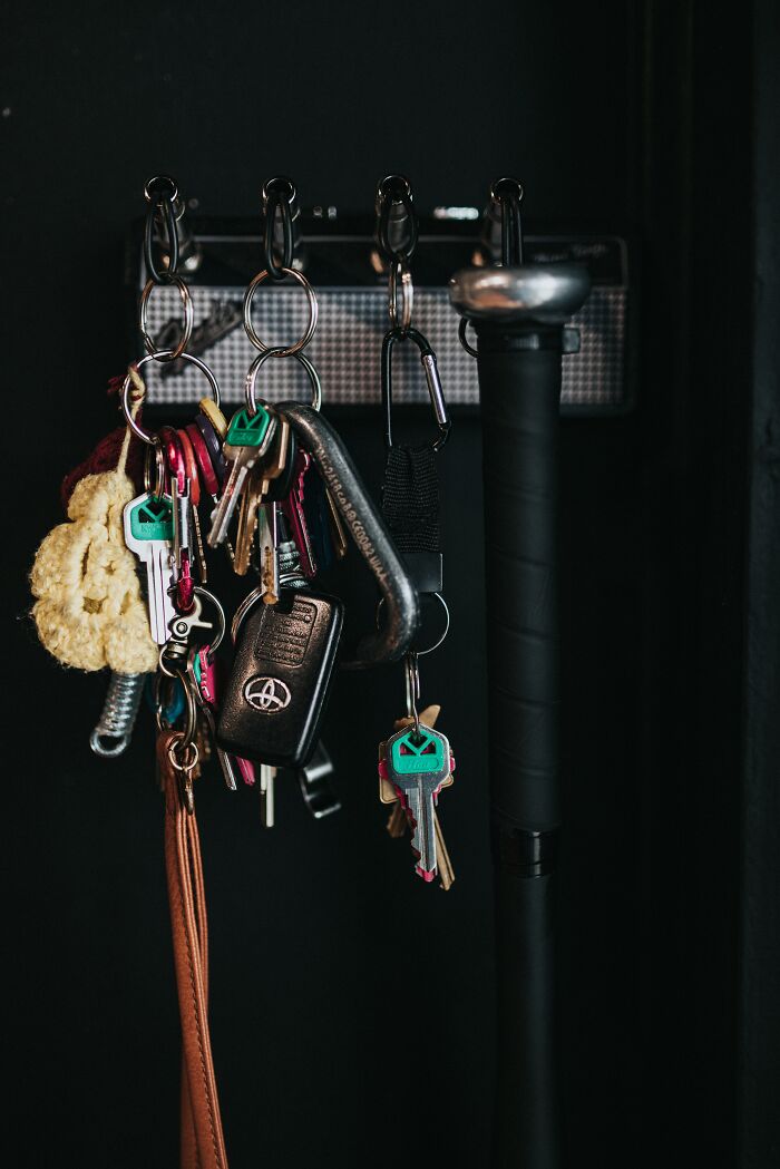 Multiple sets of keys and a key fob hanging on hooks against a dark background in a home entryway.