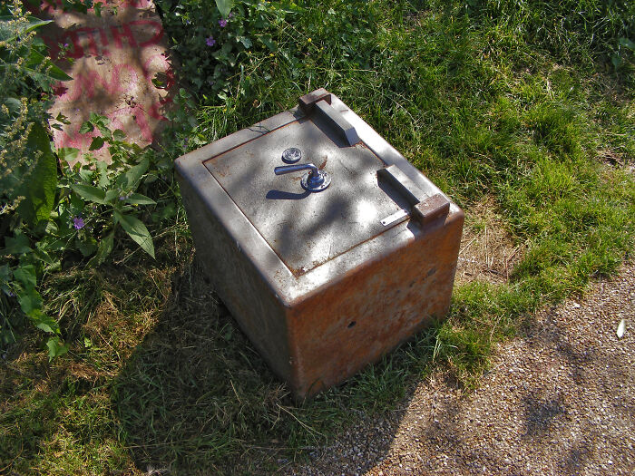 Old rusty safe placed outdoors on grass, illustrating places to never hide your stuff according to ex-burglars’ tips.