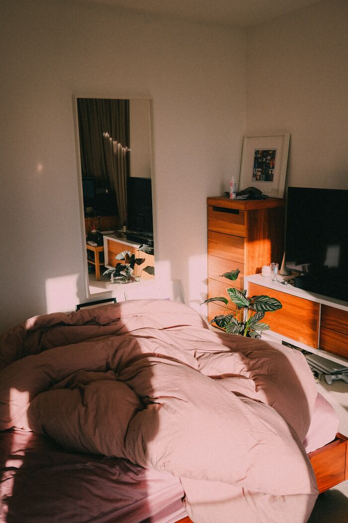 Sunlit bedroom with unmade bed, wooden furniture, mirror, and plants illustrating where burglars say not to hide your stuff.