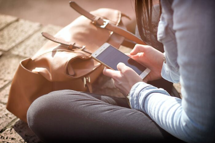 Person holding a smartphone next to a brown leather bag, illustrating tips from ex-burglars on where not to hide valuables.