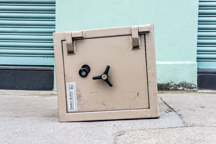 Old beige safe with combination lock placed outdoors on concrete ground, illustrating secure hiding tips from ex-burglars.