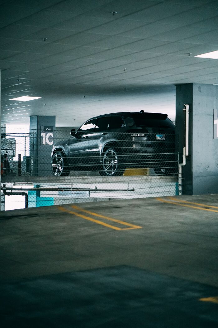 Black SUV parked in a dimly lit parking garage with chain-link fencing on level 10 for secure storage tips.