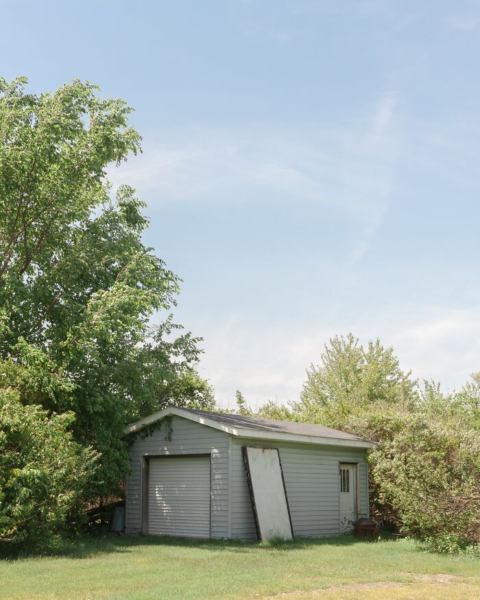 Small gray storage shed surrounded by trees and bushes, illustrating places burglars say you should never hide your stuff.
