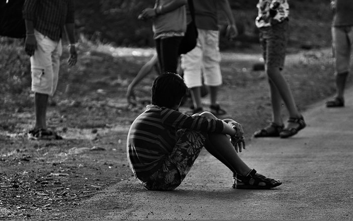 Child labeled gifted sits alone on a road while other children stand nearby in an outdoor setting.