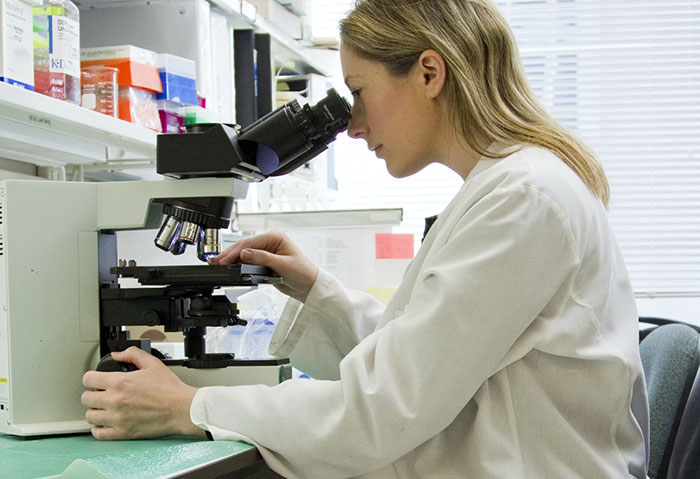 Woman labeled gifted using a microscope in a lab setting, illustrating life experiences of gifted individuals.