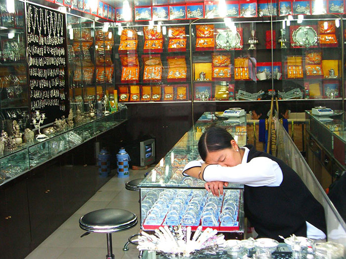 Young woman resting in a jewelry store, surrounded by glass cases filled with various silver and gold items, labeled gifted concept.