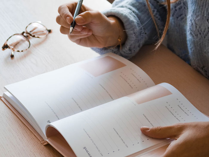 Person holding pen and writing in planner, representing people who grew up labeled as gifted sharing life experiences.