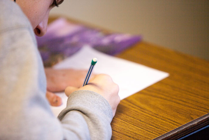 Student labeled as gifted writing with a pencil on paper at a wooden desk in a focused learning environment.
