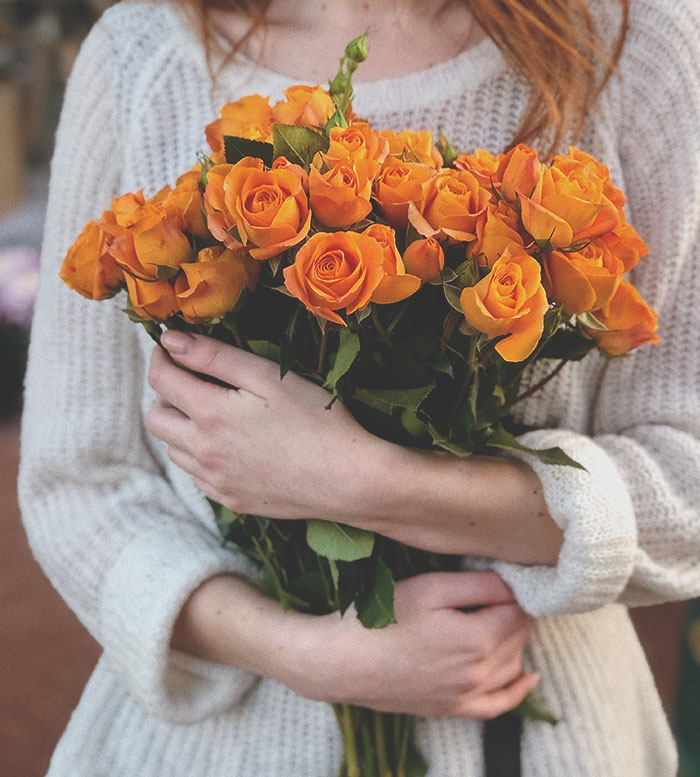 Person in cozy sweater holding a bouquet of orange roses symbolizing secret good deeds and kindness revealed.