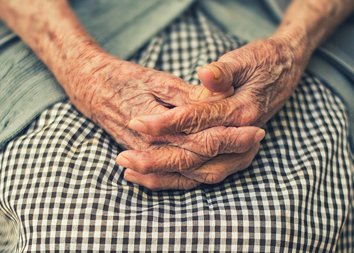 Elderly hands resting on a checkered skirt, symbolizing good deeds kept in secret and acts of kindness.