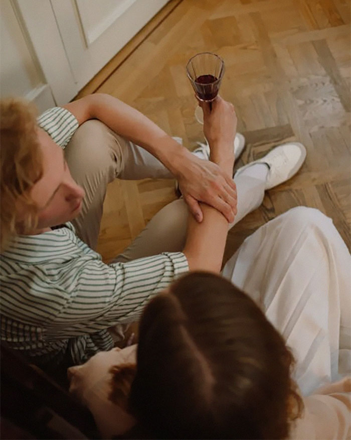 Couple sitting on wooden floor, holding hands and sharing a glass of wine, illustrating married life insights.