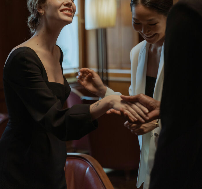 Two women smiling and shaking hands, demonstrating useful social tips to help connect with others in a group setting.