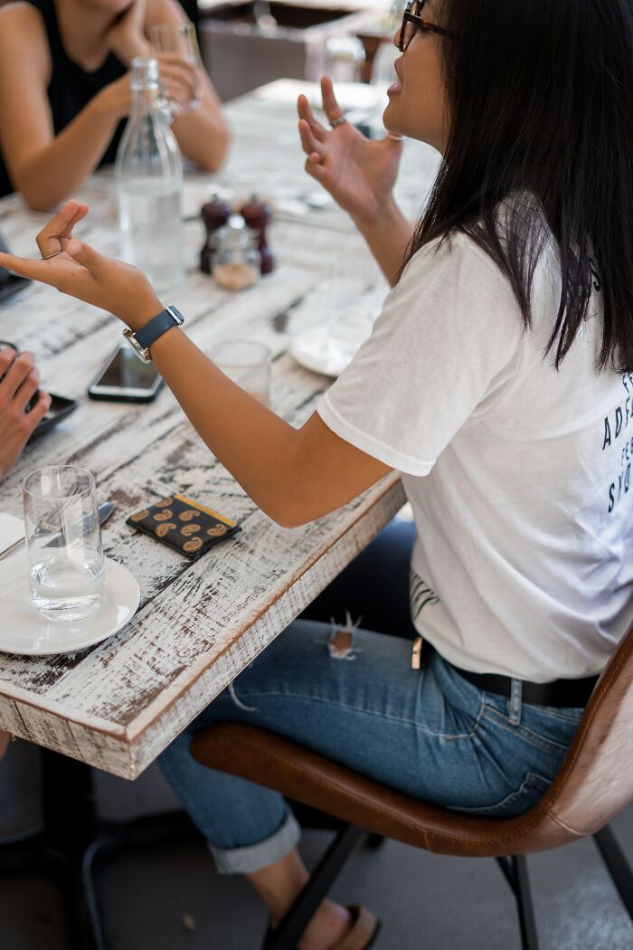 Woman in glasses and white shirt sharing social tips to help connect with others during a casual group conversation.