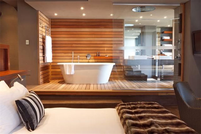 Modern home trends featuring open-concept bathroom design with wood paneling and glass walls in a contemporary bedroom setting.