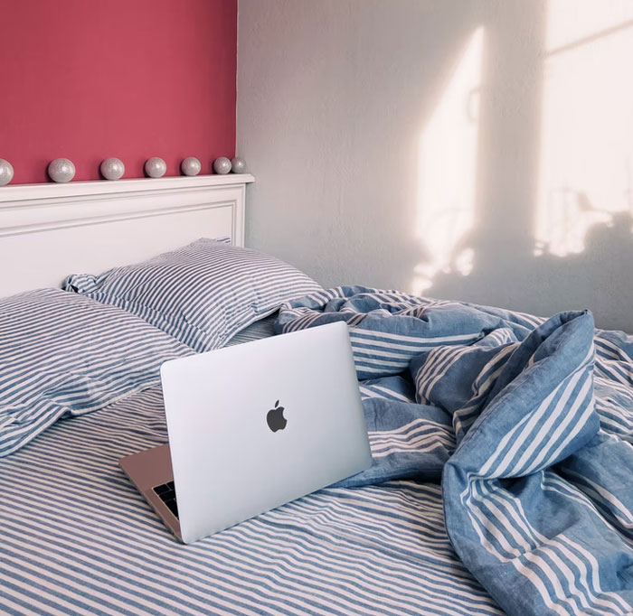 Laptop on a bed with striped bedding in a modern bedroom, illustrating popular modern home trends found annoying.