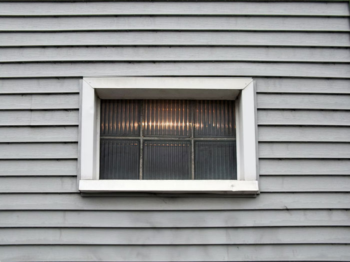 Small textured window set in plain gray siding, illustrating one of the modern home trends found annoying by many.