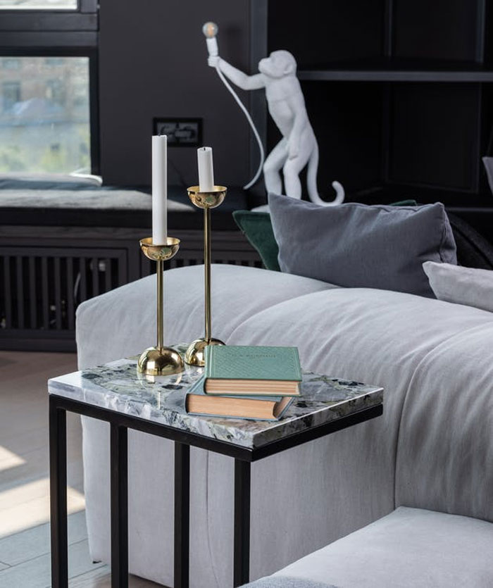 Modern home trends shown with marble side table, brass candlesticks, and decorative monkey lamp in a stylish living room.
