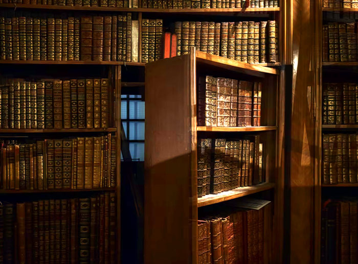 Hidden bookshelf door in a cozy room filled with antique leather-bound books, showing a unique modern home trend feature.