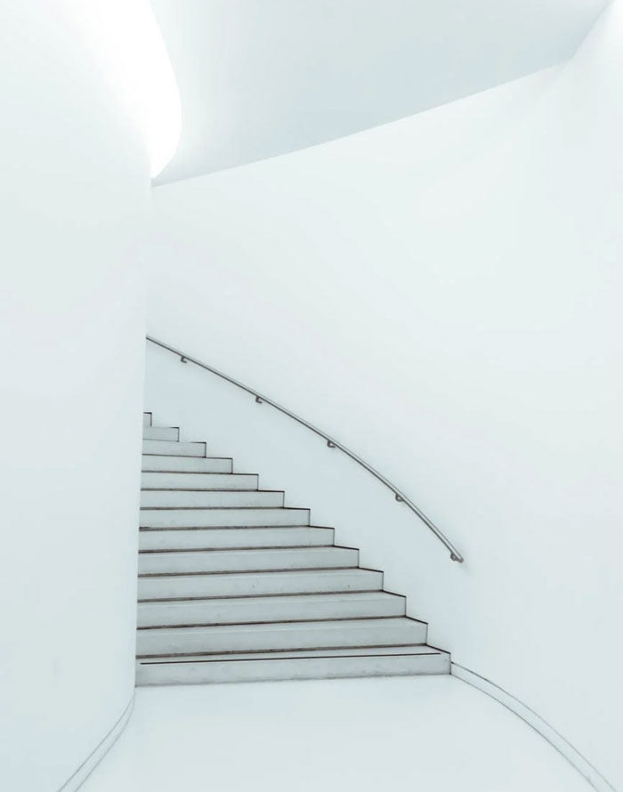 Minimalist modern home staircase with curved handrail and clean white walls showcasing current home trends.