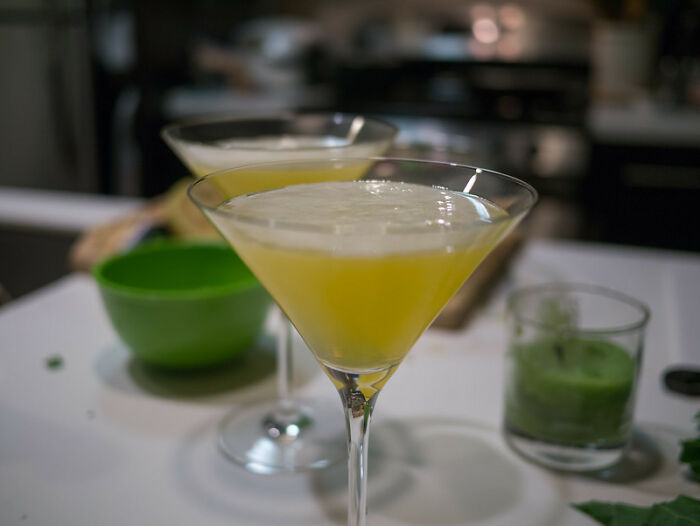 Two yellow cocktails in martini glasses on a bar counter, bartenders sharing drink orders insights online.