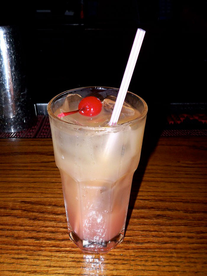 Cocktail glass with ice, cherry, and a straw on a wooden bar counter, related to bartenders and drink orders.
