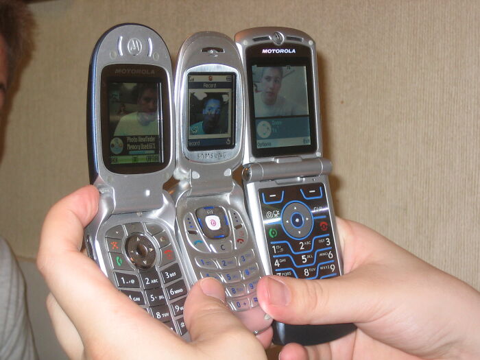 Three flip phones held side by side showing video calls in an online group chat with lawyers sharing moments.