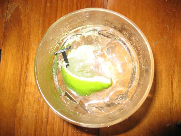 Glass with ice, lime wedge, and stir stick on wooden surface, illustrating bartenders online group drink orders insights.