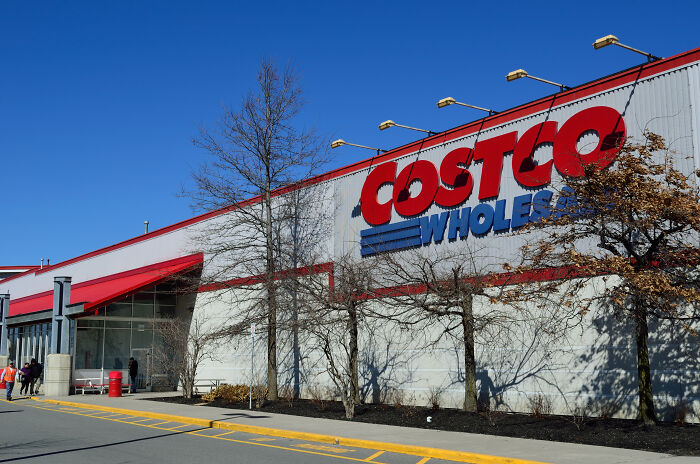 Costco exterior with clear blue sky, a few people outside, and leafless trees in front of the building.