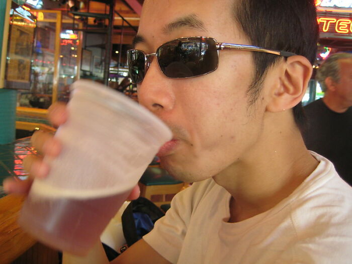Man wearing sunglasses drinking beer inside a bar with bartenders in this online group sharing drink order insights.