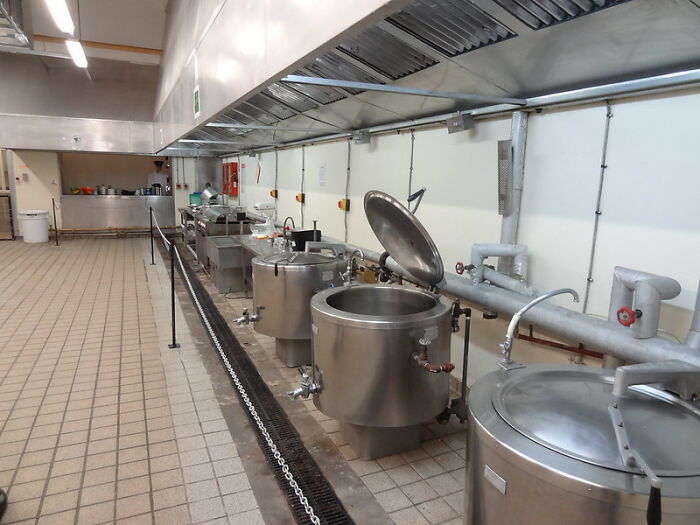 Industrial prison kitchen with large stainless steel cooking pots and equipment in a clean tiled area.
