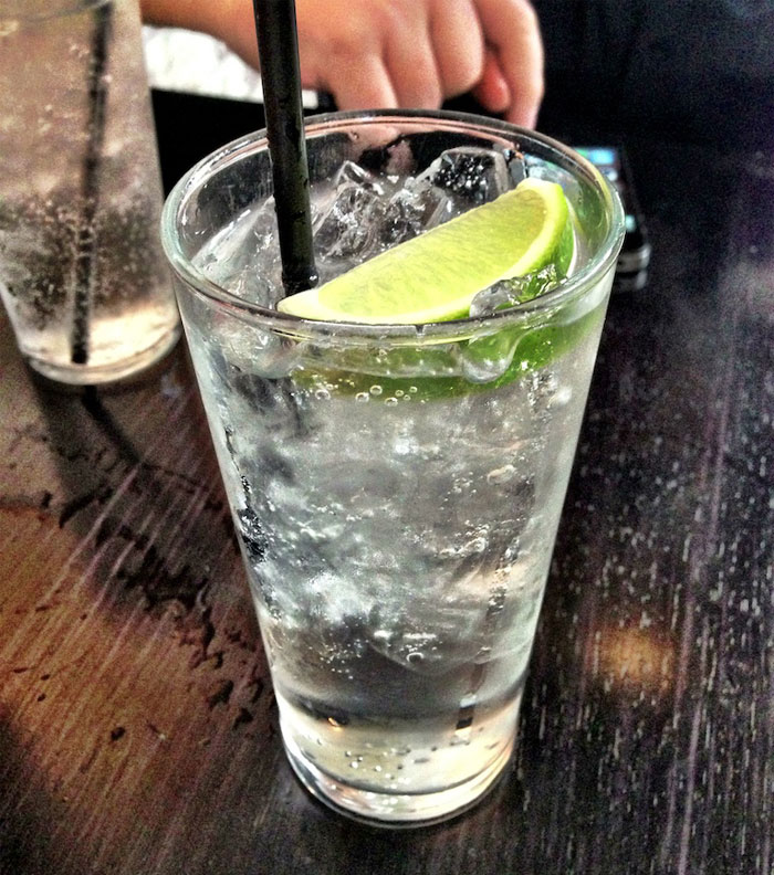 Glass of sparkling drink with lime and ice on a wooden table, bartenders sharing drink orders insights online.