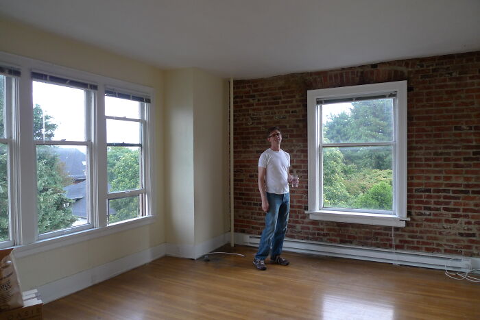Man in a white shirt and jeans stands in an empty room with wooden floors and large windows, lawyers online group concept.
