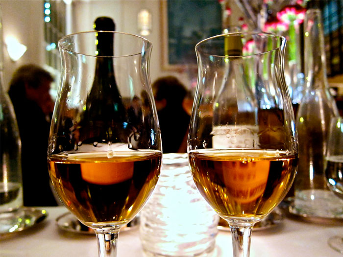 Two glasses of amber drinks on a table with a blurred bar scene, highlighting bartenders in online group insights.