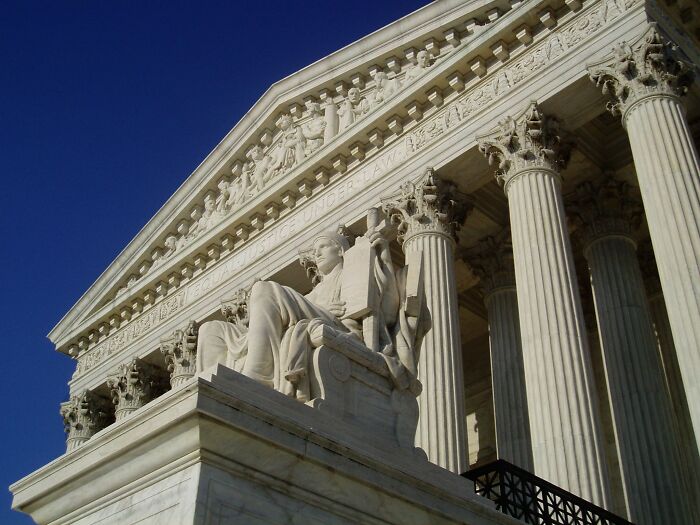 Statue of justice outside a classical courthouse with tall columns under a clear blue sky representing lawyers.