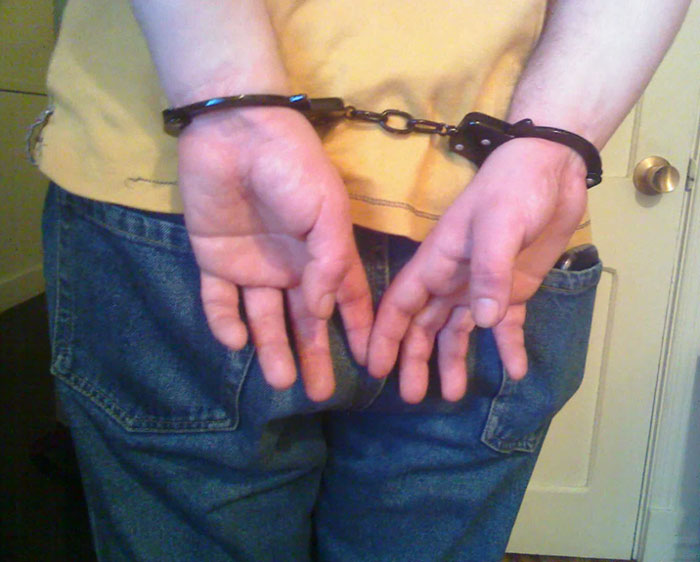 Person wearing handcuffs behind their back, illustrating challenges former prisoners and their families face during incarceration.