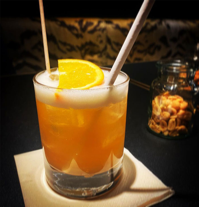 Cocktail with orange slice and straws on a table with nuts in the background reflecting bartenders drink orders insights.