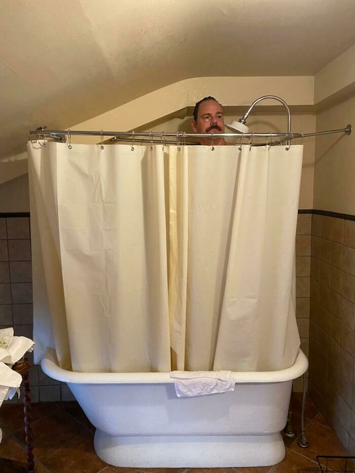 Man stands awkwardly in a small bathtub with a low ceiling; an example of awful home interiors.