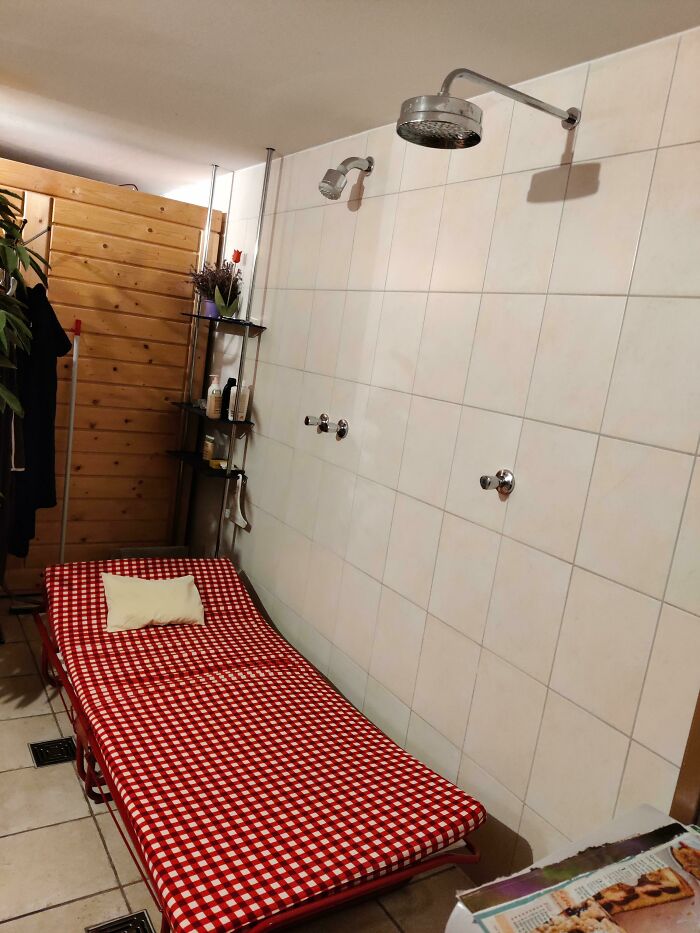 Awful interior design choice with a red checkered bed under a showerhead in a tiled room.